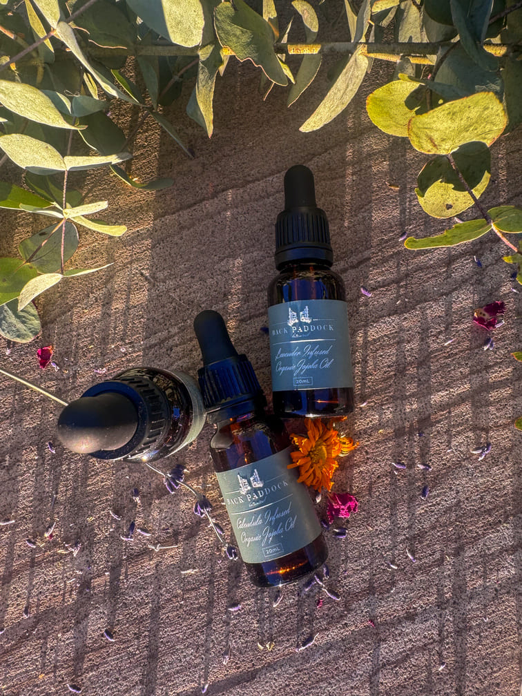 Three dropper bottles of jojoba oils with labels on a textured surface with leaves and flowers.