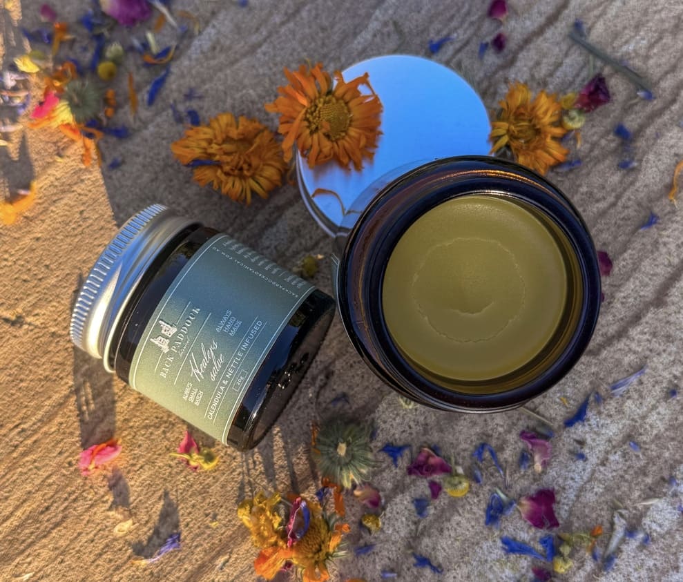Calendula and Nettle infused salve in a jar on a board with flower petals