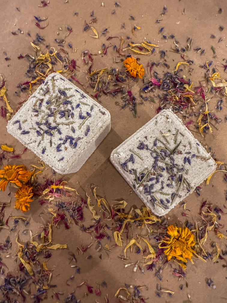 Two cube bath bombs with dried flowers on a brown surface