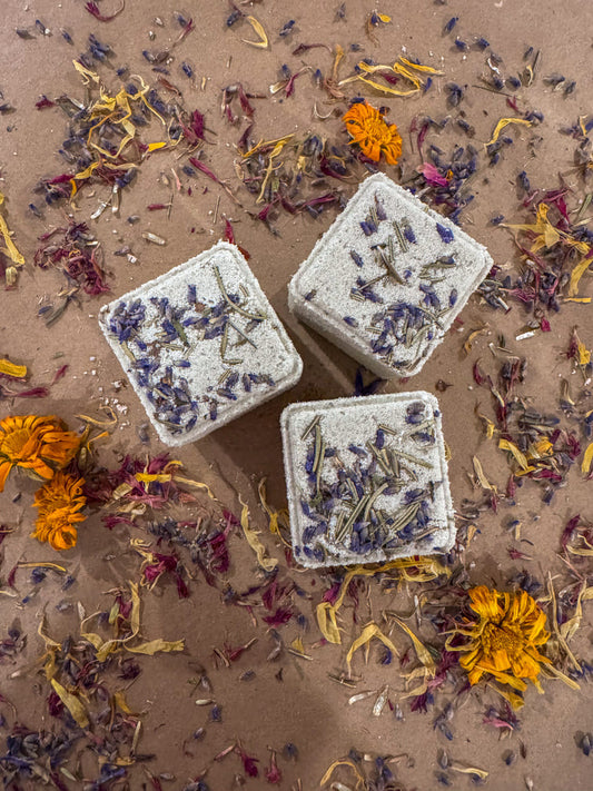 Three cubes bath bombs with dried flowers on a sandy background