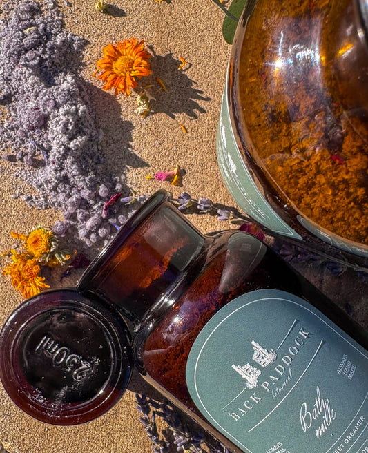 Two amber glass bottles with labels on a textured surface with flowers and herbs.