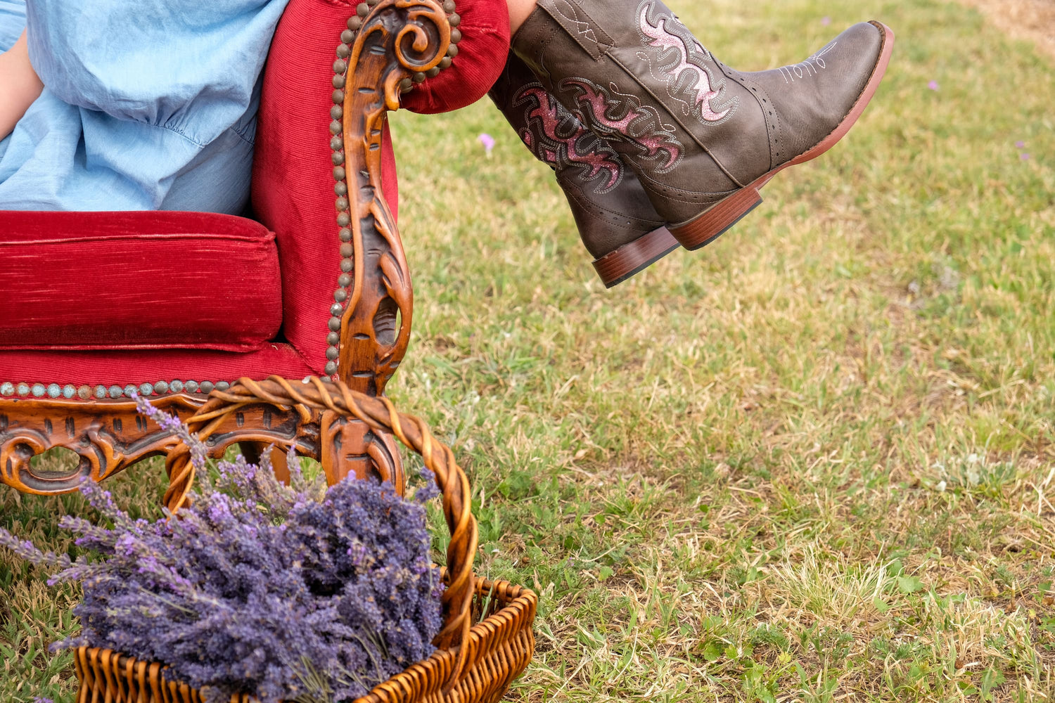Person wearing cowboy boots with intricate designs, sitting on a red chair outdoors.