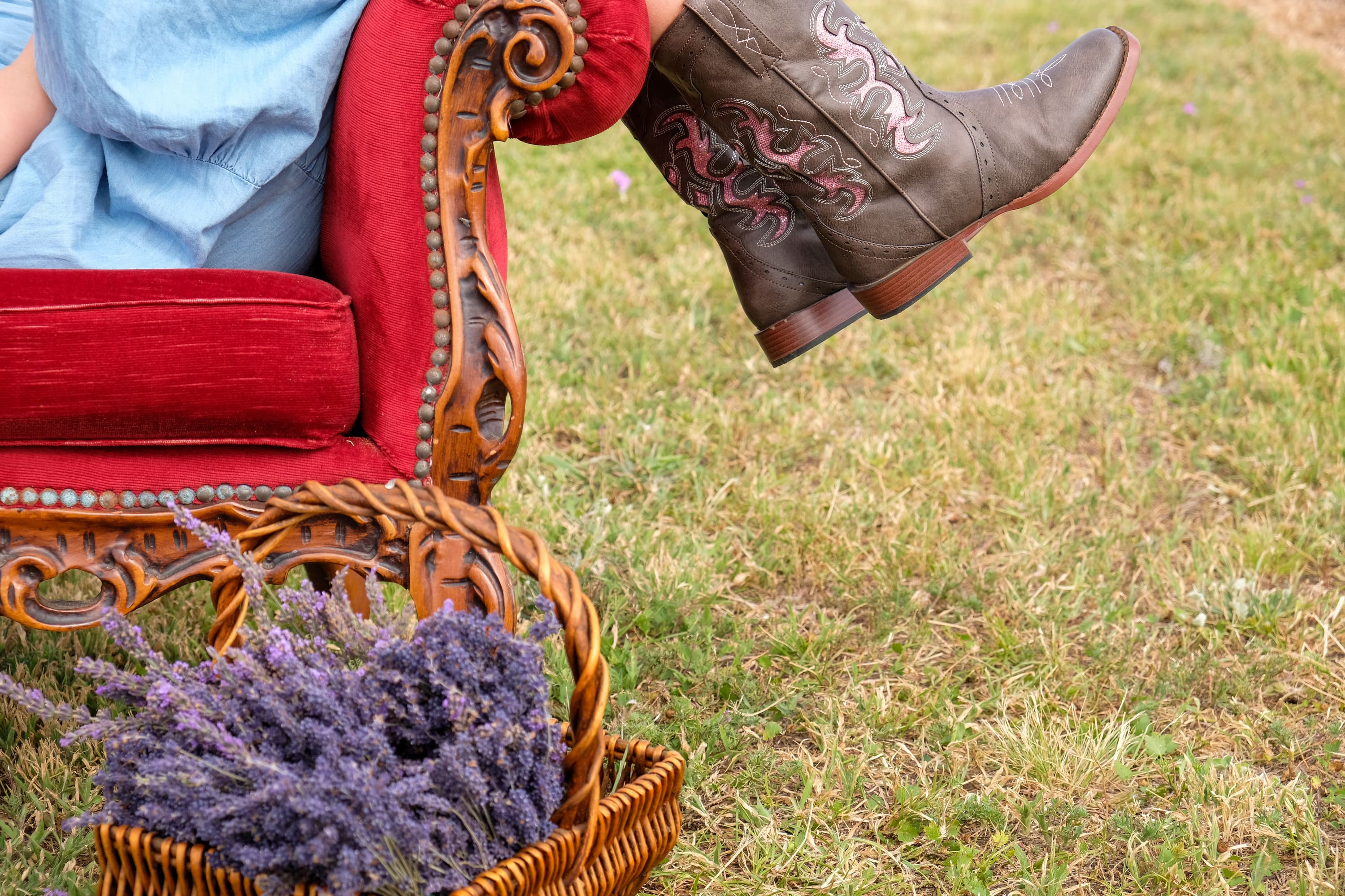 Person wearing cowboy boots with intricate designs, sitting on a red chair outdoors.