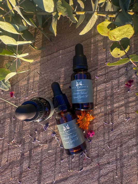 Three dropper bottles of jojoba oil with labels on a textured surface with leaves and flowers.