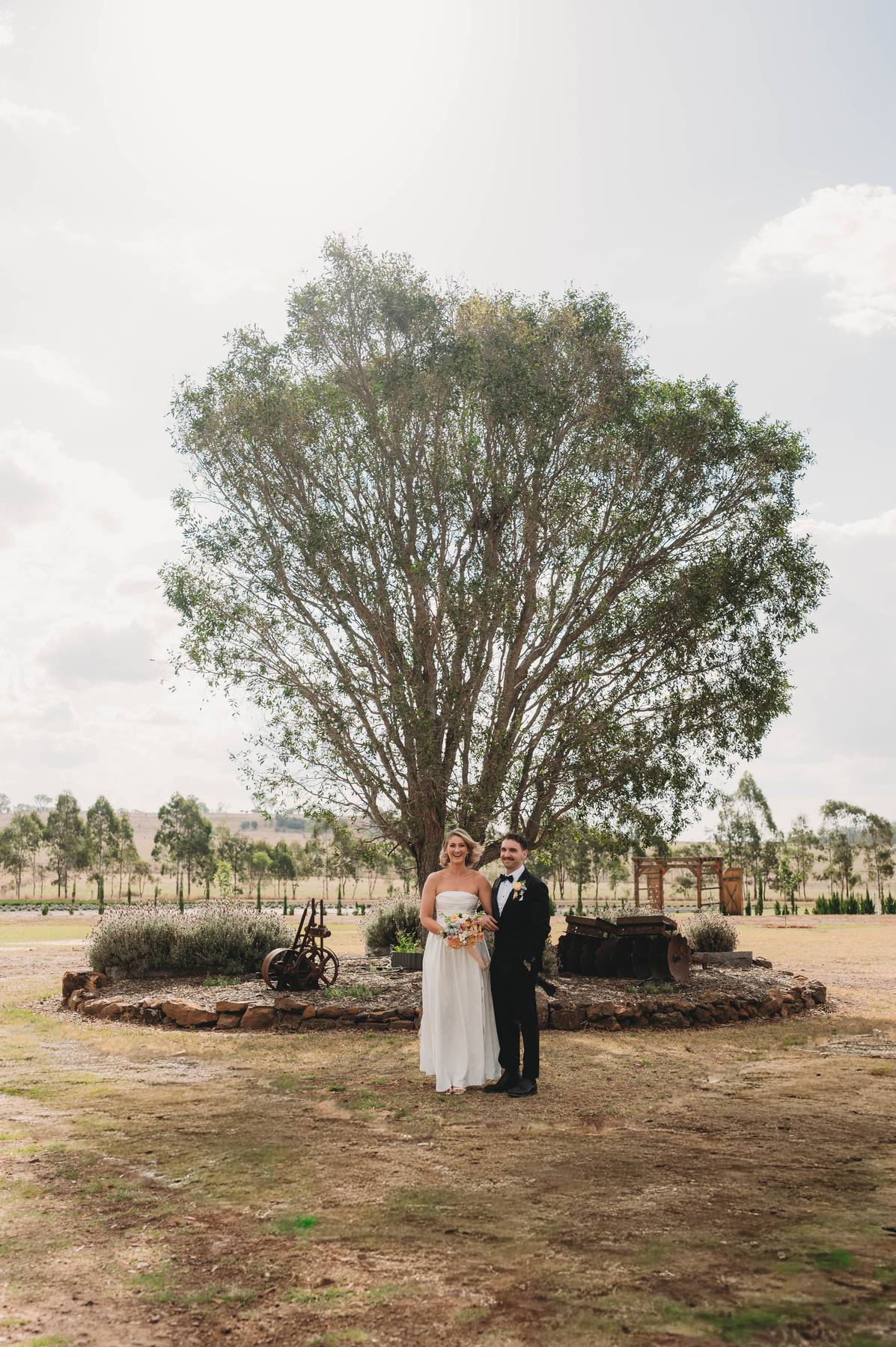 Couple standing in front of a large tree with a scenic background