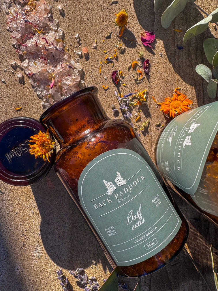 Amber-colored bottle with a green label saying secret garden bath salts.