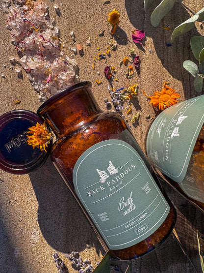 Amber-colored bottle with a green label saying secret garden bath salts.