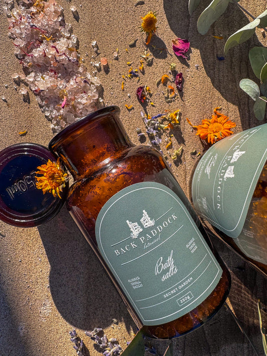 Amber-colored bottle with a green label saying secret garden bath salts.