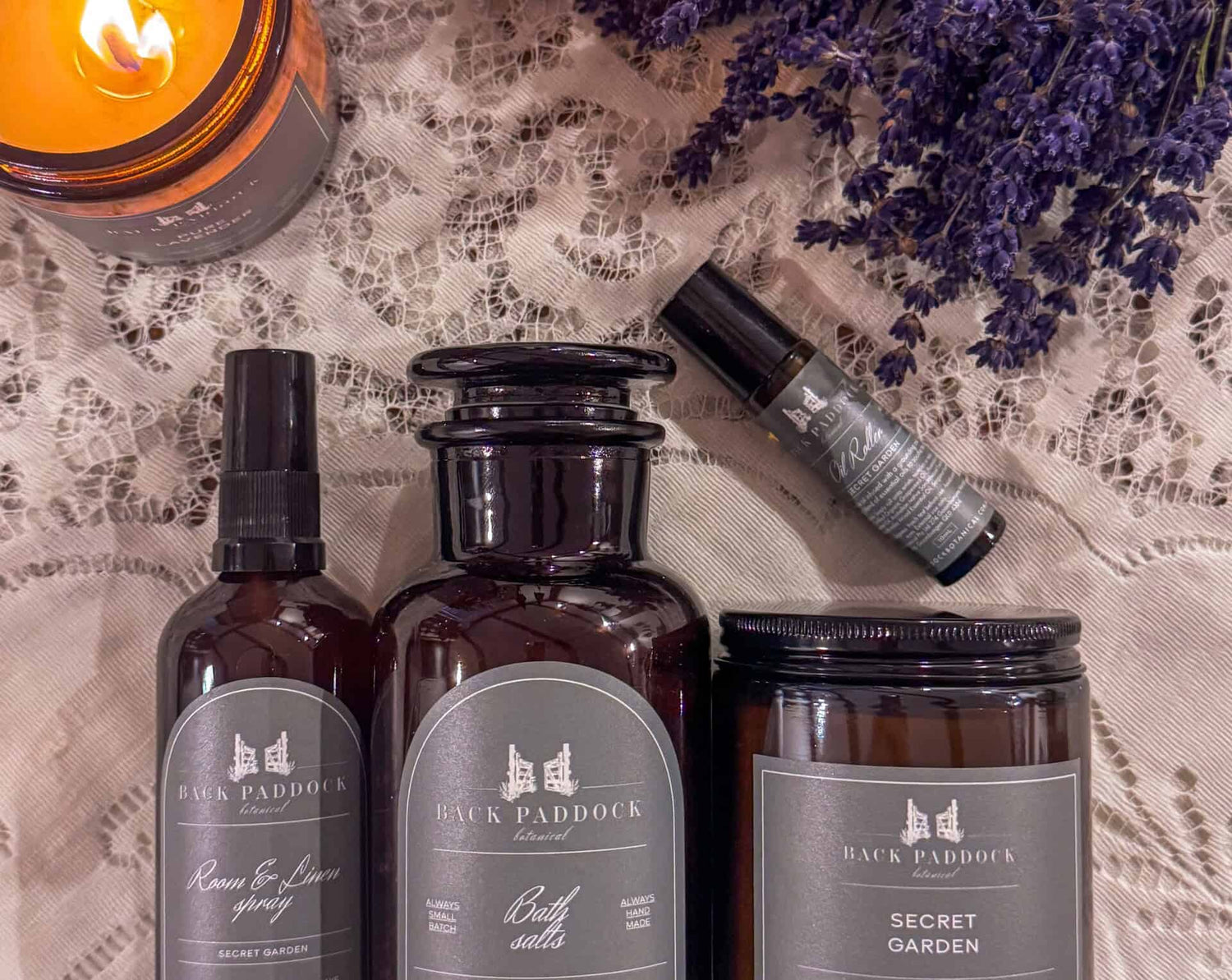 Three bottles and a candle with 'Back Paddock' branding on a textured fabric background.