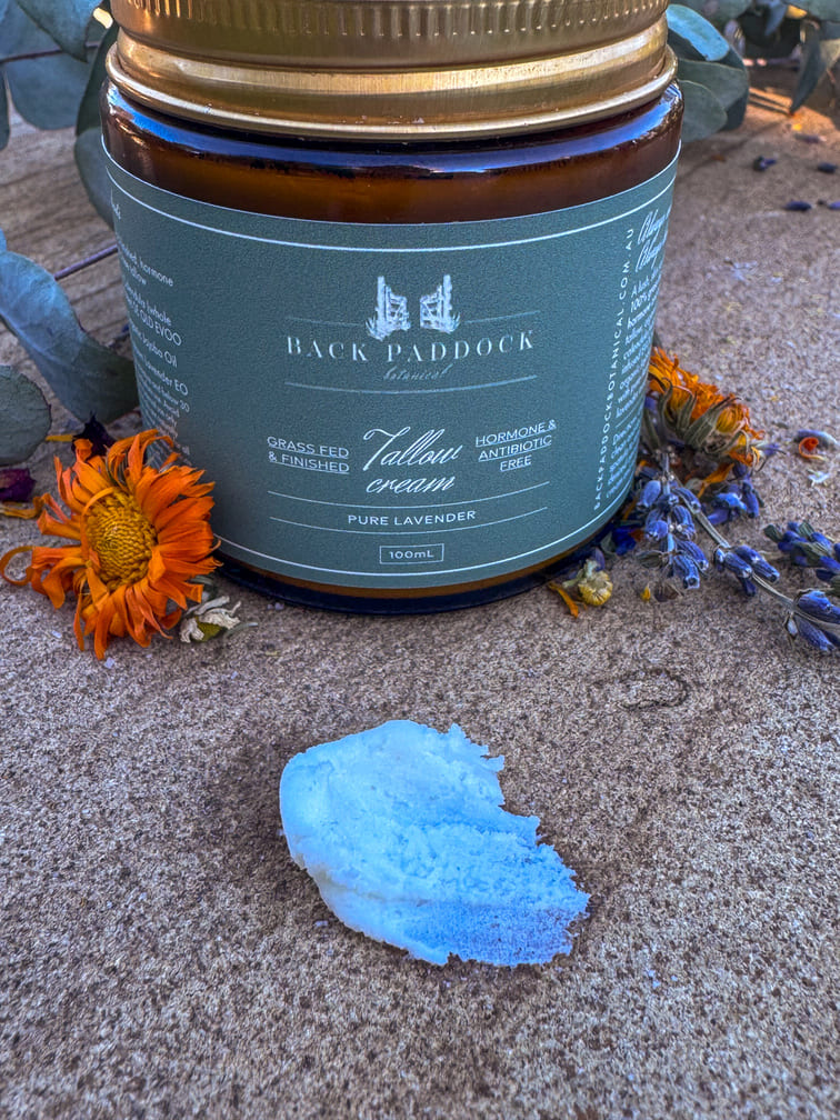 Jar of Back Paddock Tallow Cream with a small amount of cream on a textured surface with flowers.