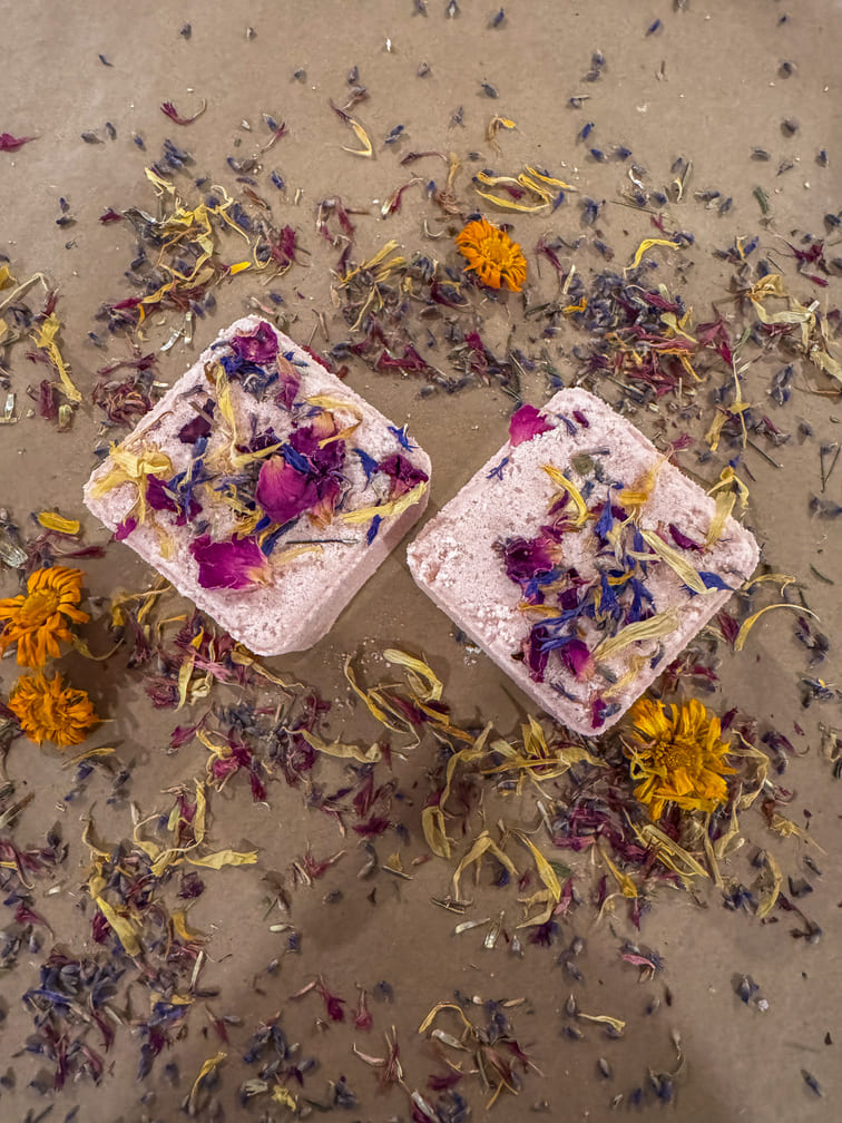 Two pink bath bombs with dried flowers on a sandy background