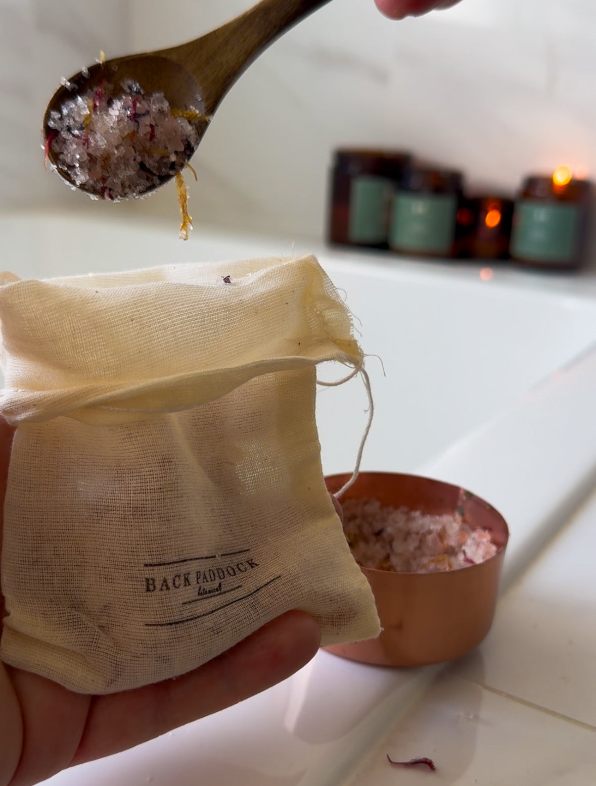 Hand holding a tea bag labeled 'Back Paddock' with a wooden spoon and small bowl in the background.