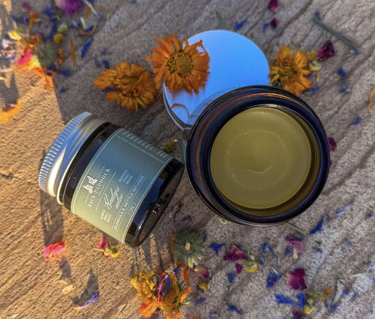 Two jars of healers salve with floral decorations on a textured surface