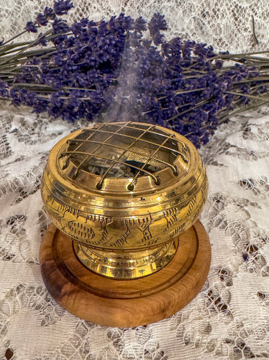 Brass incense burner with wooden base on a lace tablecloth with lavender flowers.