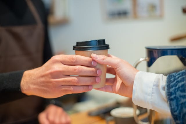 A hand passing a takeaway coffee to another