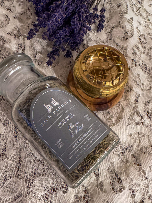 Glass bottle of lavender and rosemary loose smoke cleansing mix with a metal incense burner and imber round base.