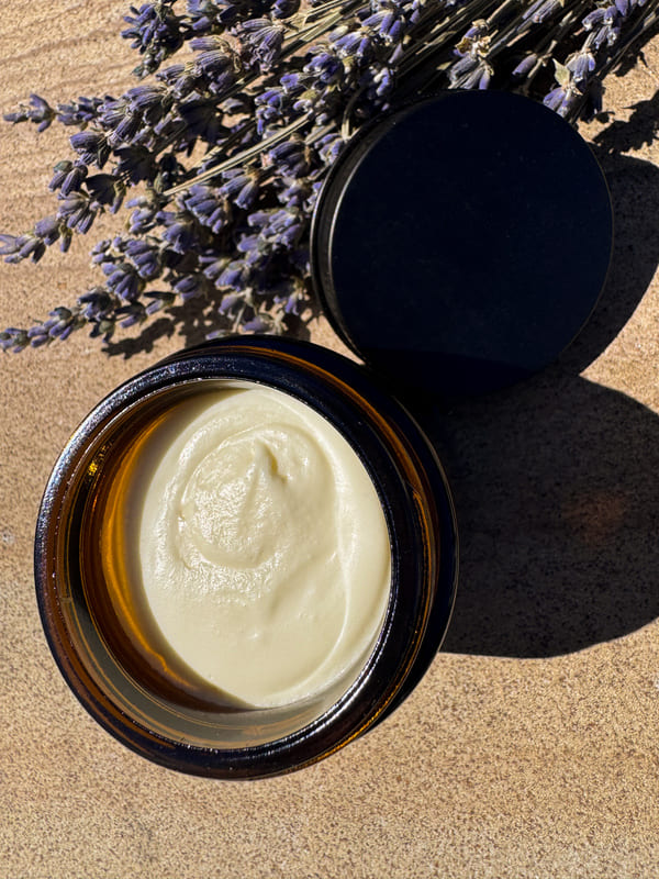 Open jar of lavender tallow cream, surrounded by lavender flowers.