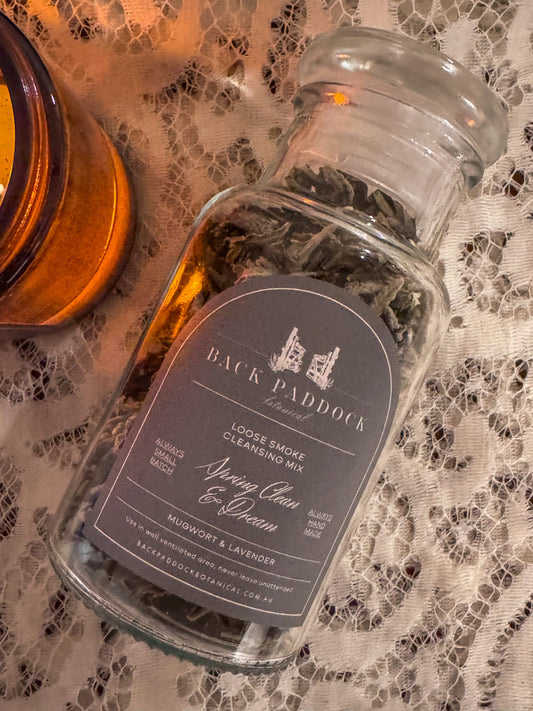 Glass bottle of Back Paddock Mugwort and Lavender Loose Smoke Cleansing Mix on a lace surface. 