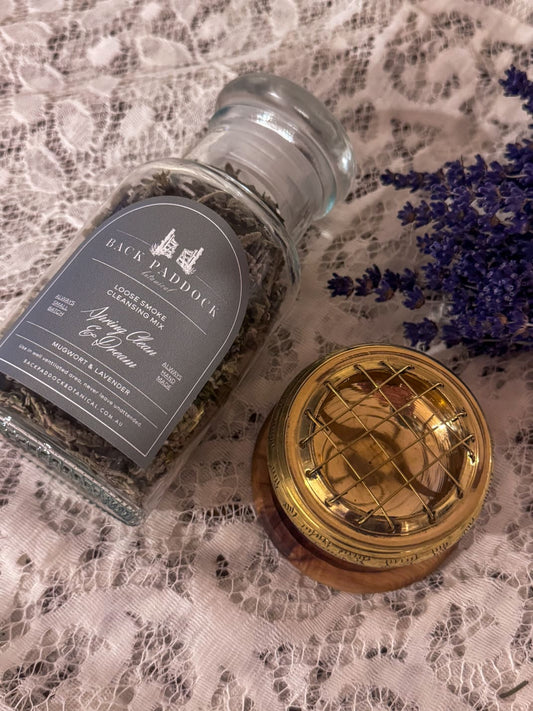 Glass jar of mugwort and lavender smoke cleansing mix with a small burner on a small timber round base.