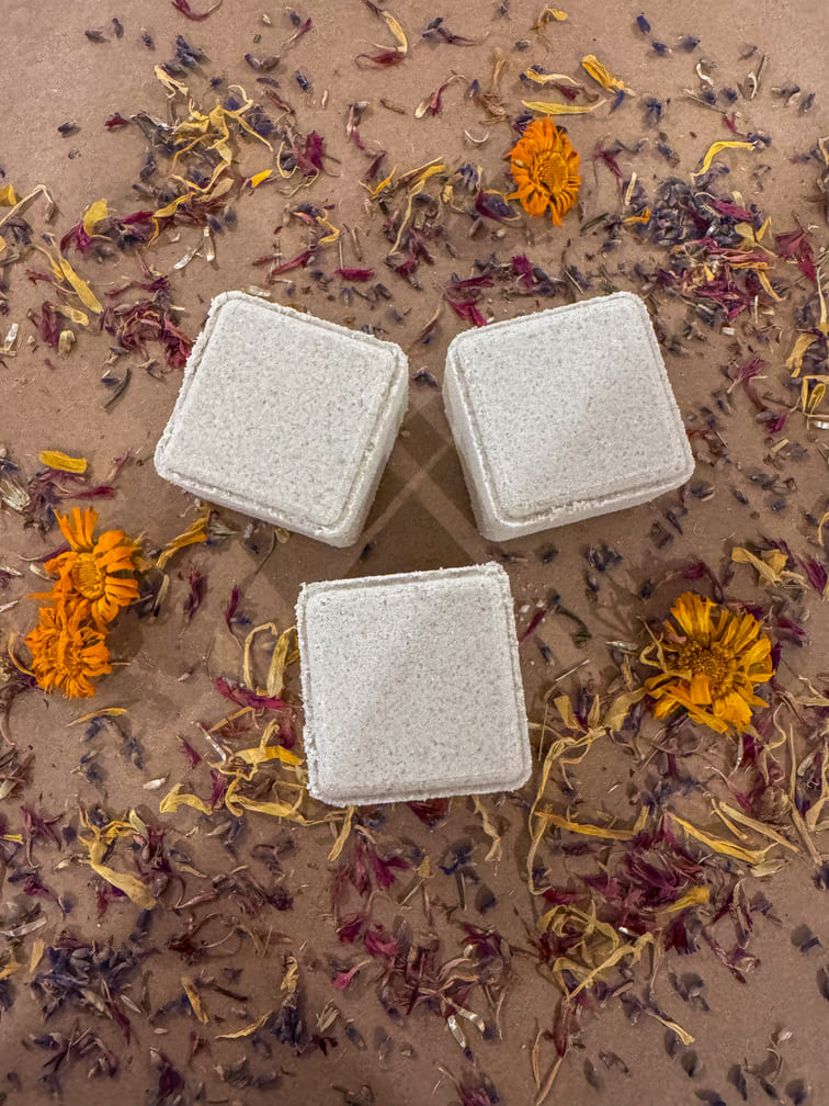 3 cube shower steamers infused with lavender, blue cypress, bush balm mint and buddha wood essential oils, on a bed of dried flowers.