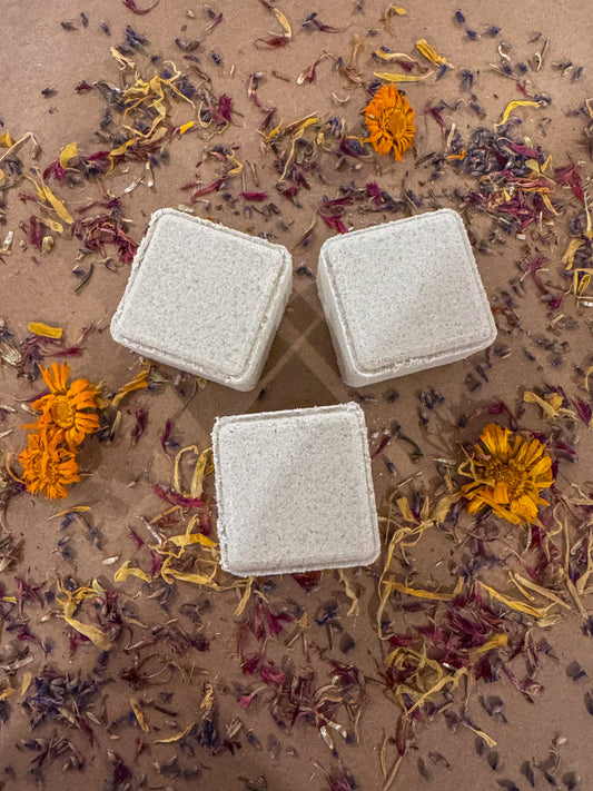 3 cube shower steamers infused with lavender, blue cypress, bush balm mint and buddha wood essential oils, on a bed of dried flowers.