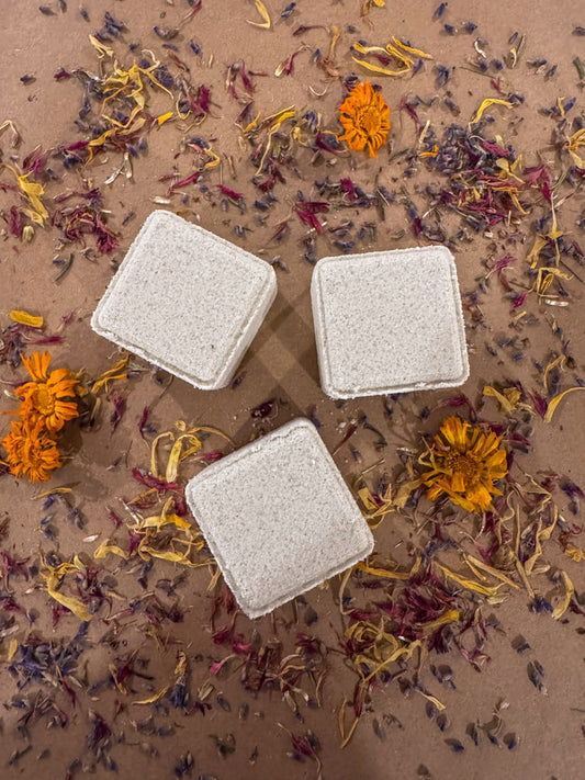 Three cube shower steamers infused with lavender and rosemary essential oils, on a bed of dried flowers.