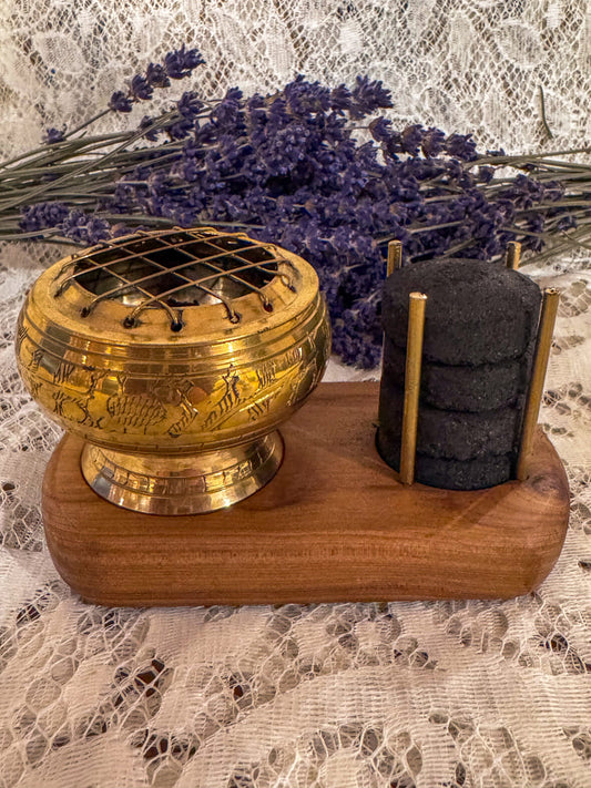 Decorative cleansing burner with charcoal sticks on a wooden base, lavender flowers in the background.