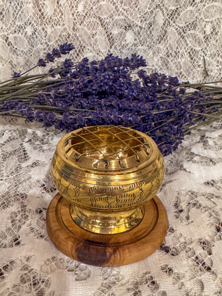 Gold incense burner object on a wooden base with lavender flowers on a lace background
